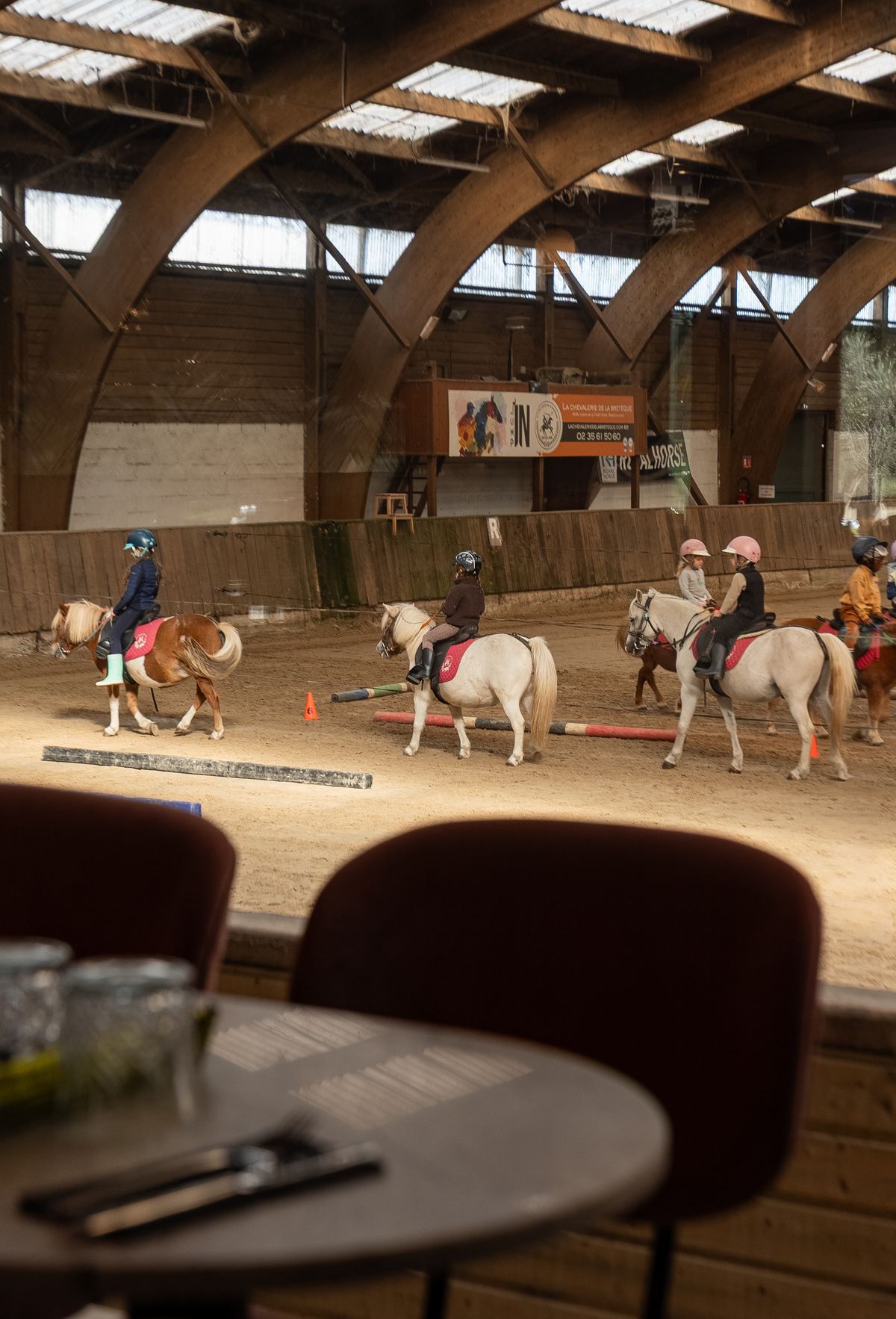 La salle de Mamma Mia ouverte sur le manège, cavaliers et poneys en arrière-plan